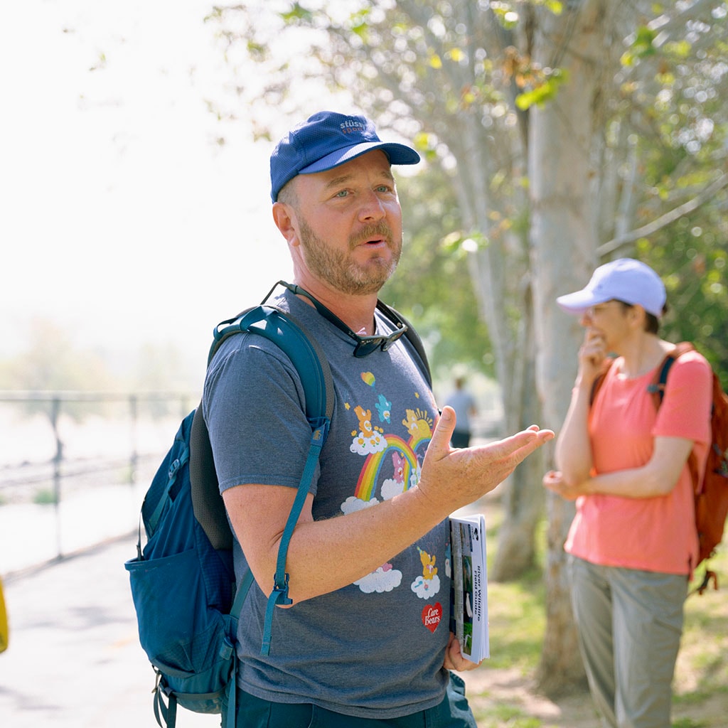 A person in a blue shirt and blue hat talks to a group outside