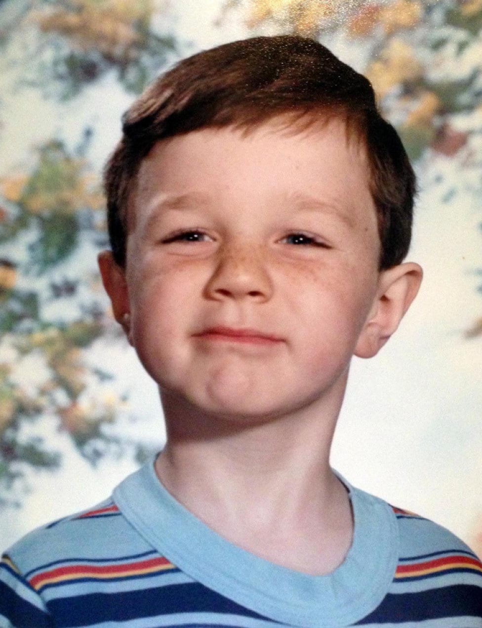 A school portrait of a young boy with freckles wearing a striped shirt