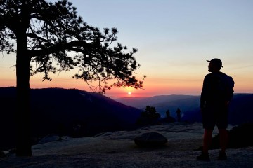 A person in silhouette watches a sunset