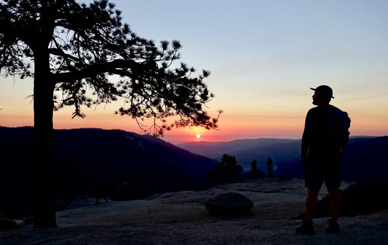 A person in silhouette watches a sunset