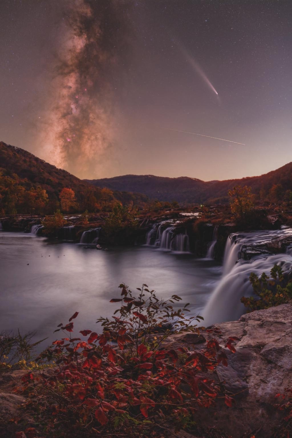 A photo of a body of water with the Milky Way and a shooting star illuminated above