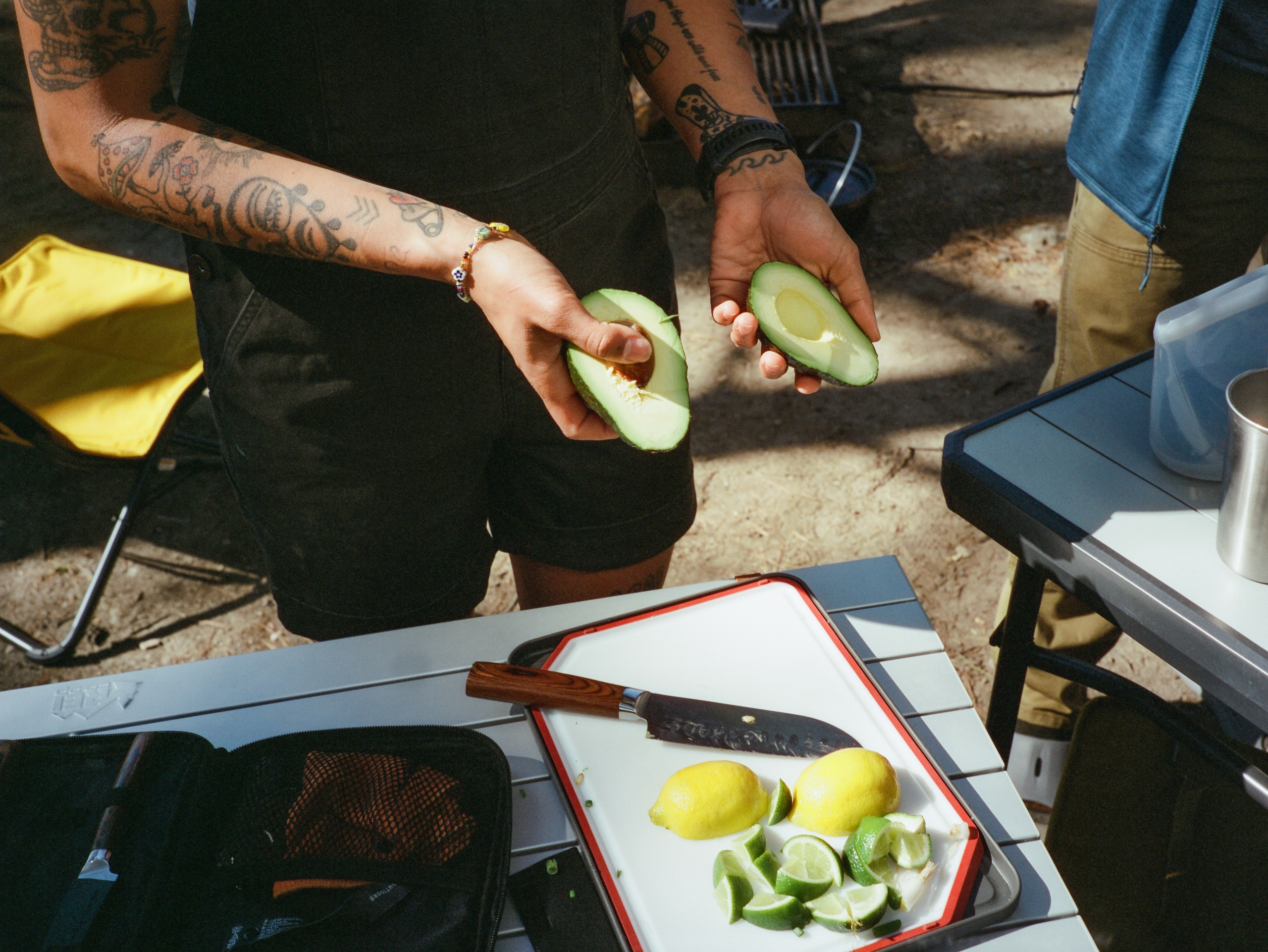 A person at a campsite slices avocado and citrus to cook a meal.