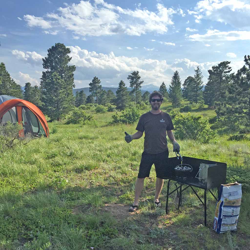 A person stands outside in behind a grill and in front of a tent