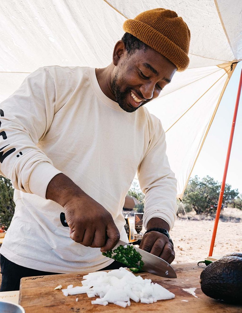 A person standing outdoors under a tarp covering cuts onions on a cutting board.