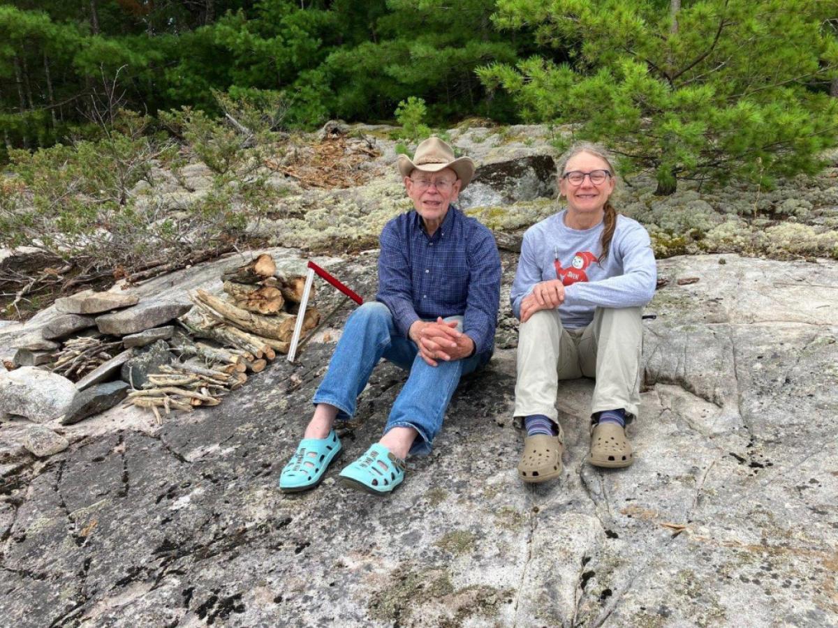 Two people sit side by side on a rock outside, with smiles on their faces