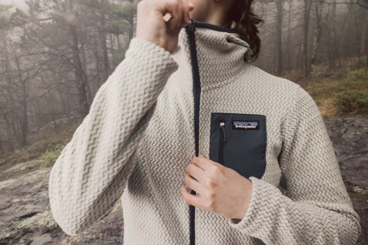 A person zips up a hoodie while in the forest.