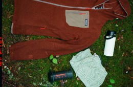 A Patagonia fleece, an AeroPress coffee maker, and a thermos are laid down on the grass.