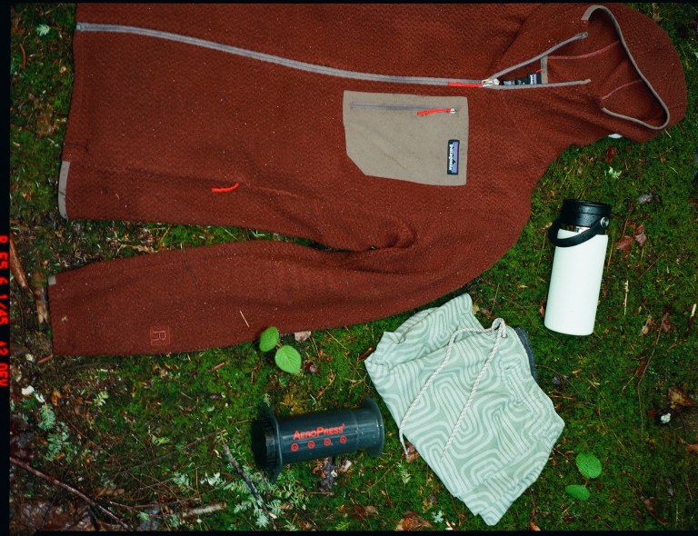 A Patagonia fleece, an AeroPress coffee maker, and a thermos are laid down on the grass.