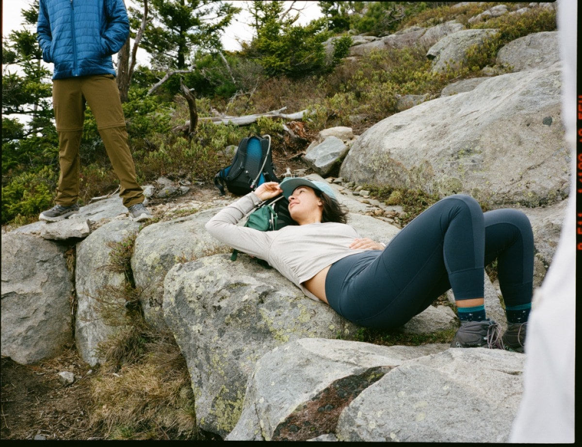 A person lays down on a rock, while another stands nearby.