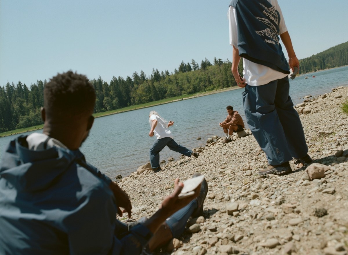Several people recreate on a rocky beach; in the middle ground, someone is skipping stones.