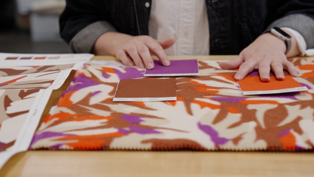 A person seen from the shoulders down sits at a table, looking through textiles and color swatches.