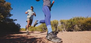 Two people running on a trail in the HOKA Challenger 8 trail-running shoes in black.