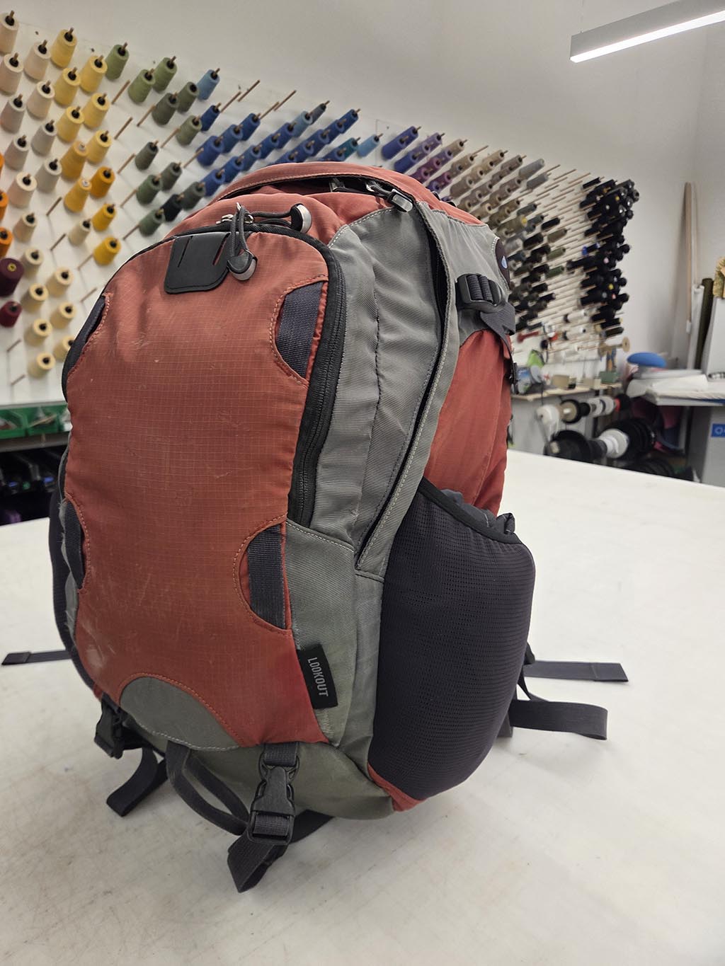 A photo of one side of a used red backpack, after it has undergone several repairs.
