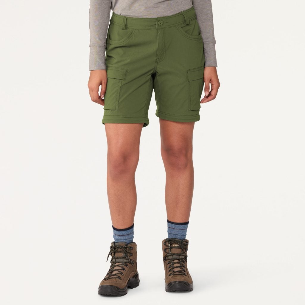 A person shown from the waist down wearing a pair of olive convertible pants that have been zipped off into shorts