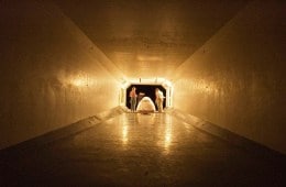 A long tunnel, at the end of which is two people standing over a tent.