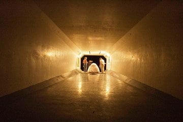A long tunnel, at the end of which is two people standing over a tent.