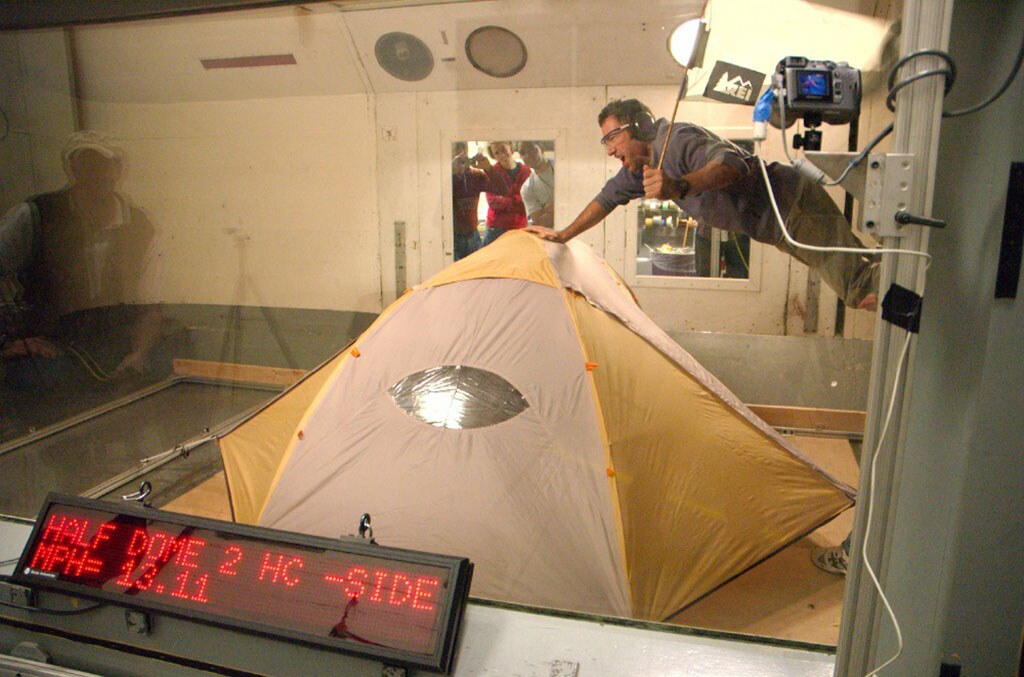 A person in a wind chamber holds the top of a tent.