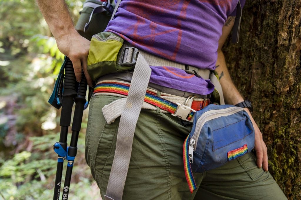 A person wearing a waistpack with a rainbow belt and patch is shown from thigh to stomach height