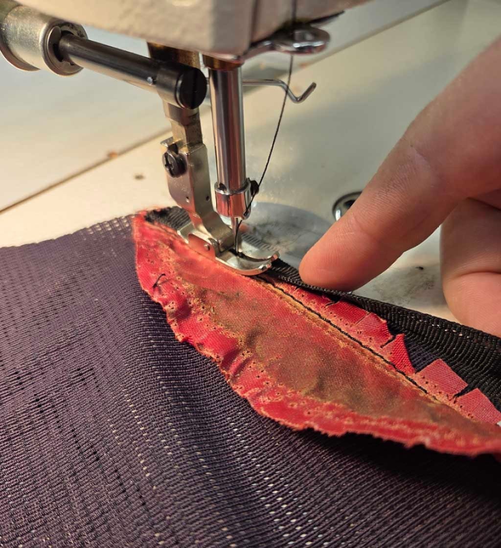 A close up of a sewing machine needle and a line of fresh stitching on an old backpack
