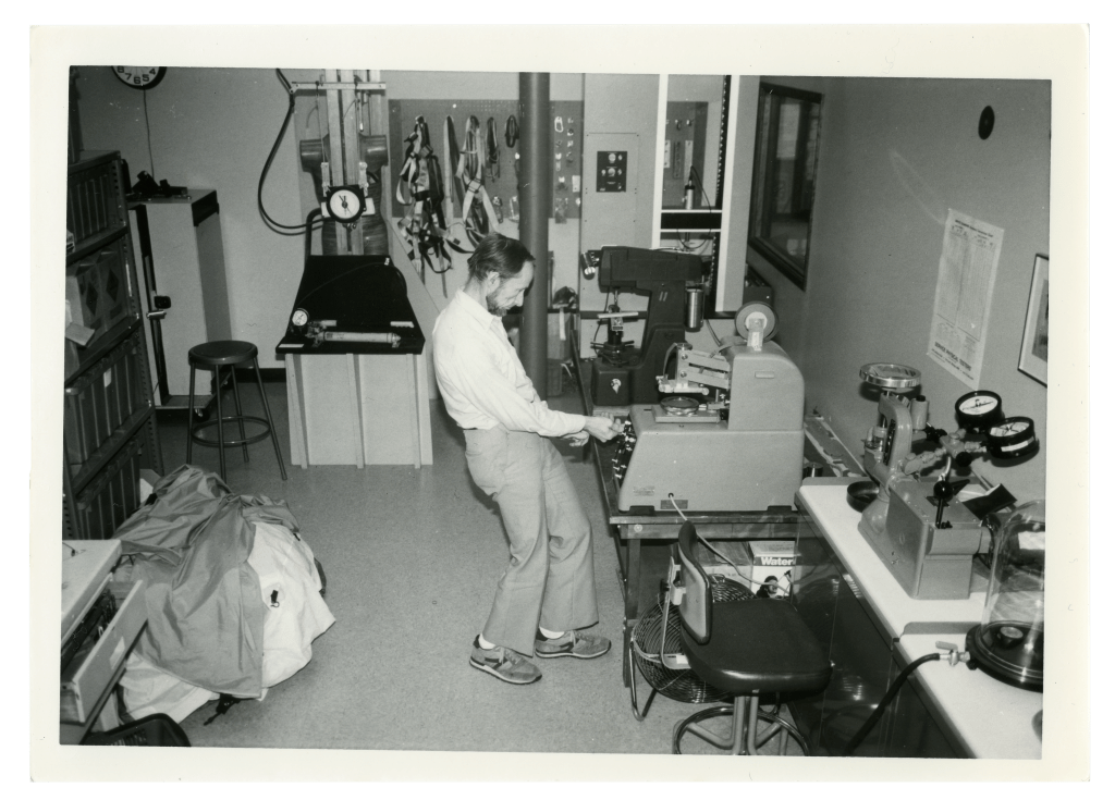 A black and white photograph featuring a laboratory and a single technician examining some results on a piece of equipment