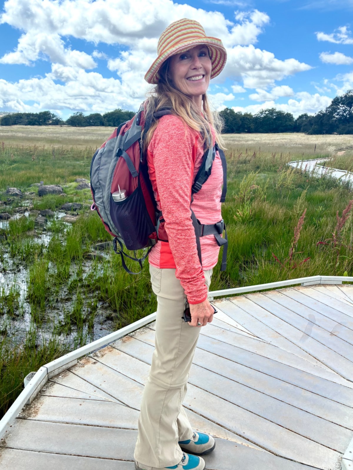 A person standing on a boardwalk trail, facing sideways and showing off their pack.