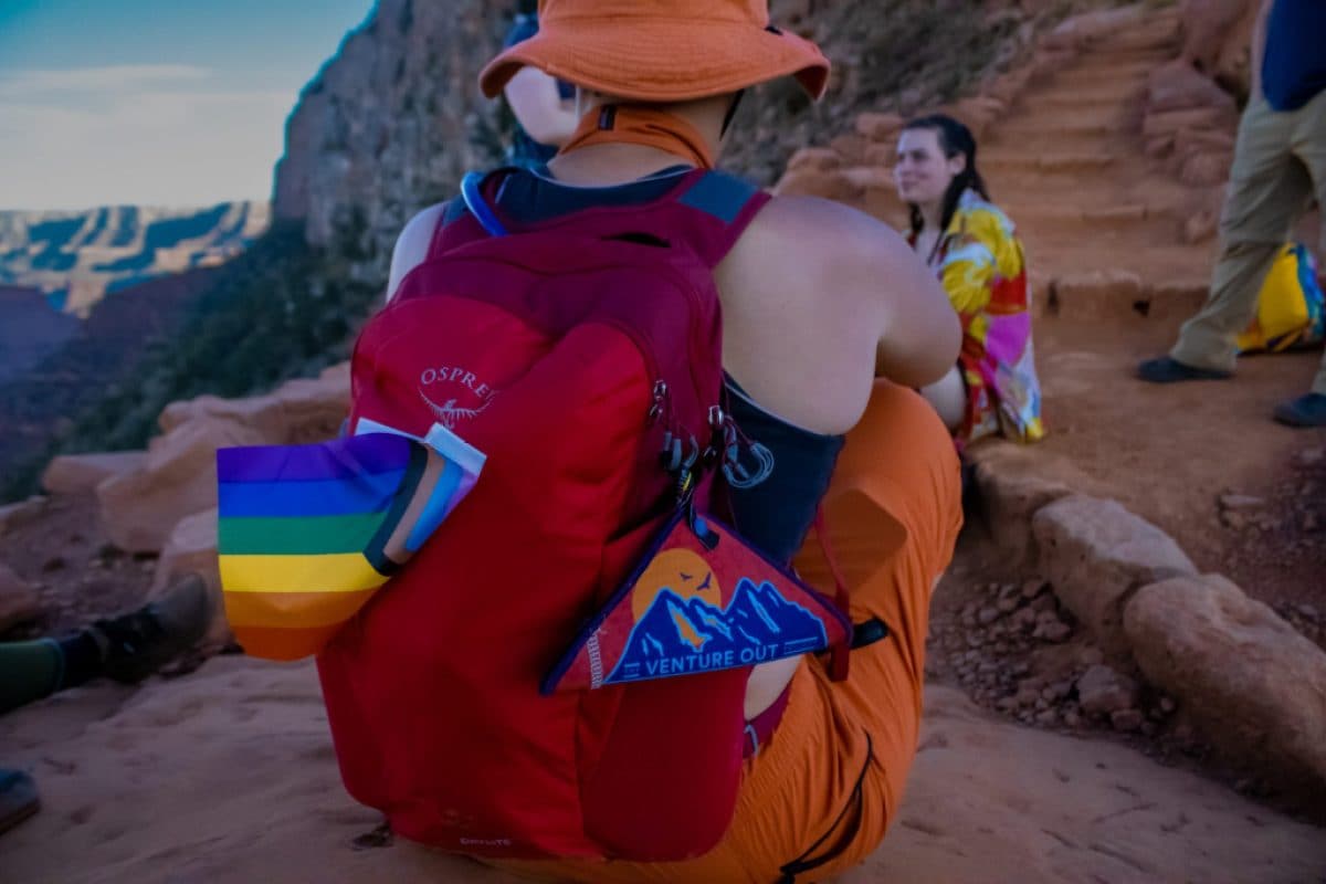 A person sits on a mountain at dusk with their back to the camera; they have a pee cloth with the Venture Out Project logo pinned to their pack