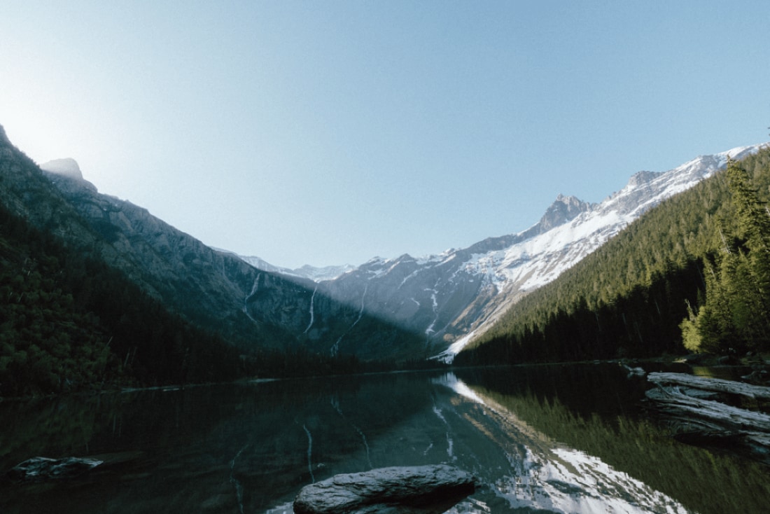 A landscape photograph from across a body of water featuring a mountain peak and pine trees in the distance