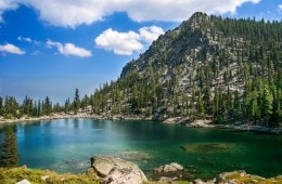 A photo of a pine-covered peak in the background behind a crystal blue lake