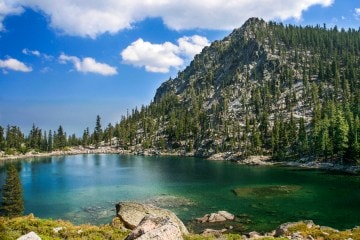 A photo of a pine-covered peak in the background behind a crystal blue lake