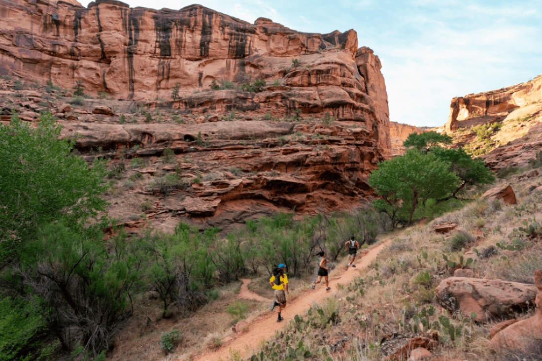 A photo of three people trail running in front of large red rock formation