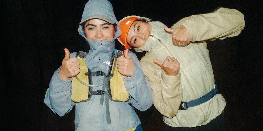 Two runners giving a thumbs of to the camera, each wearing the REI Co-op Swiftland Windshell Running Jacket in blue and yellow, respectively.