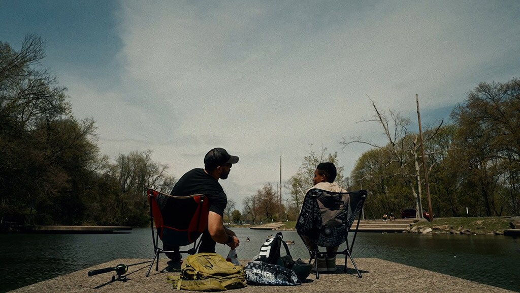 A grown man and a young boy sit side by side in camping chairs