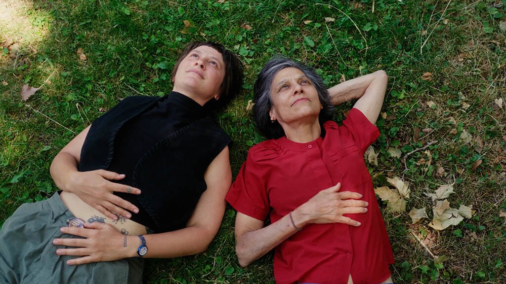 Two people of different generations lie on the grass side by side, looking up as if at the sky