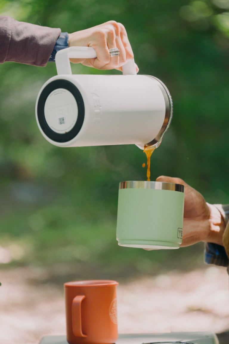 A person pours coffee from a French press into a camp mug