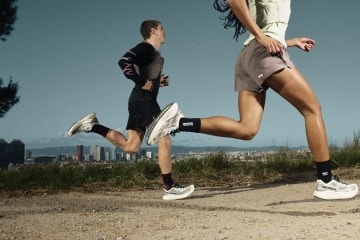 Two people running down a gravel path with a city view behind them.