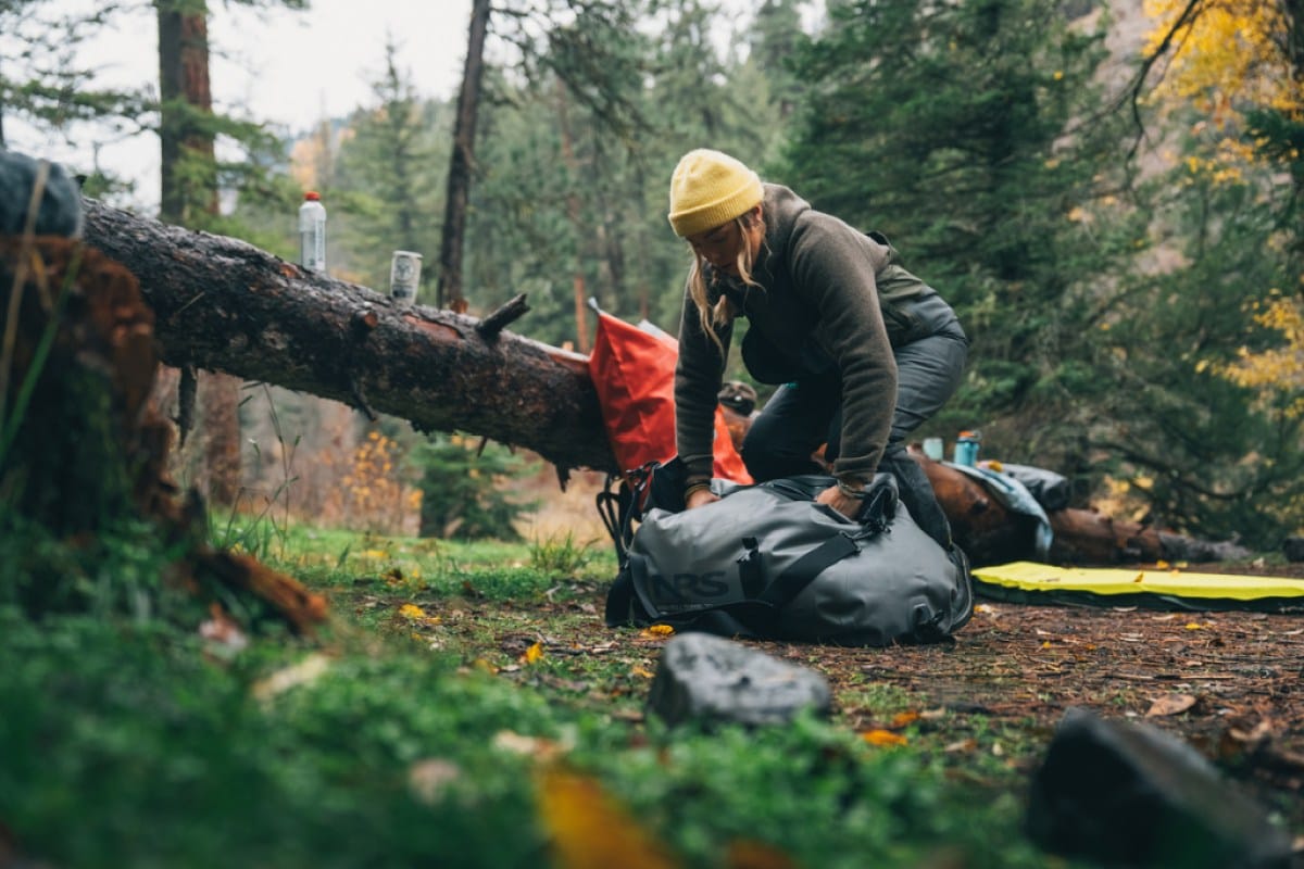 A person in a wooded area stuffs items into their dry bag.