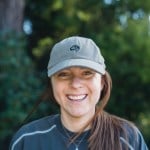 A headshot of a woman smiling, wearing a ball cap