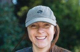 A headshot of a woman smiling, wearing a ball cap
