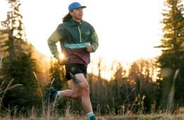 A person in a hat and windbreaker running through a forest