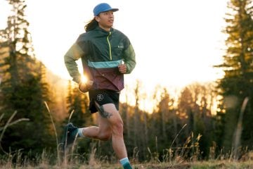 A person in a hat and windbreaker running through a forest