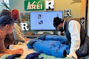 Several people gather around a design table to inspect a 1986 REI Co-op Expedition Parka