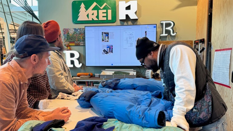 Several people gather around a design table to inspect a 1986 REI Co-op Expedition Parka
