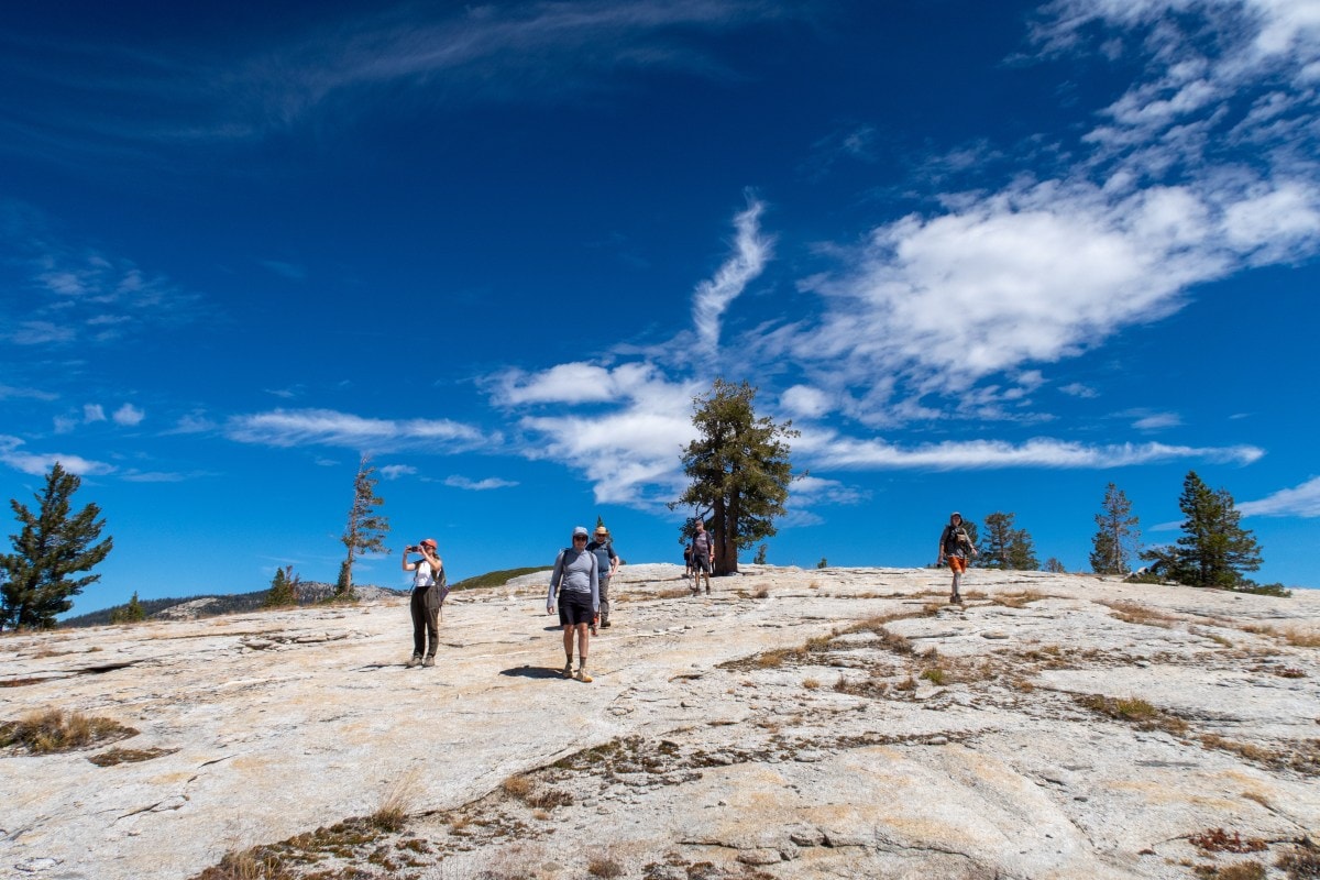 A group of five hikers descend a rocky slope in Yosemite National Park, with blue sky above them