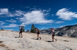 Three hikers move up a rocky slope in Yosemite National Park with blue sky behind them