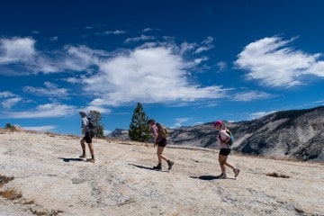 Three hikers move up a rocky slope in Yosemite National Park with blue sky behind them