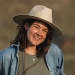 A photo of a woman smiling, wearing a white hat