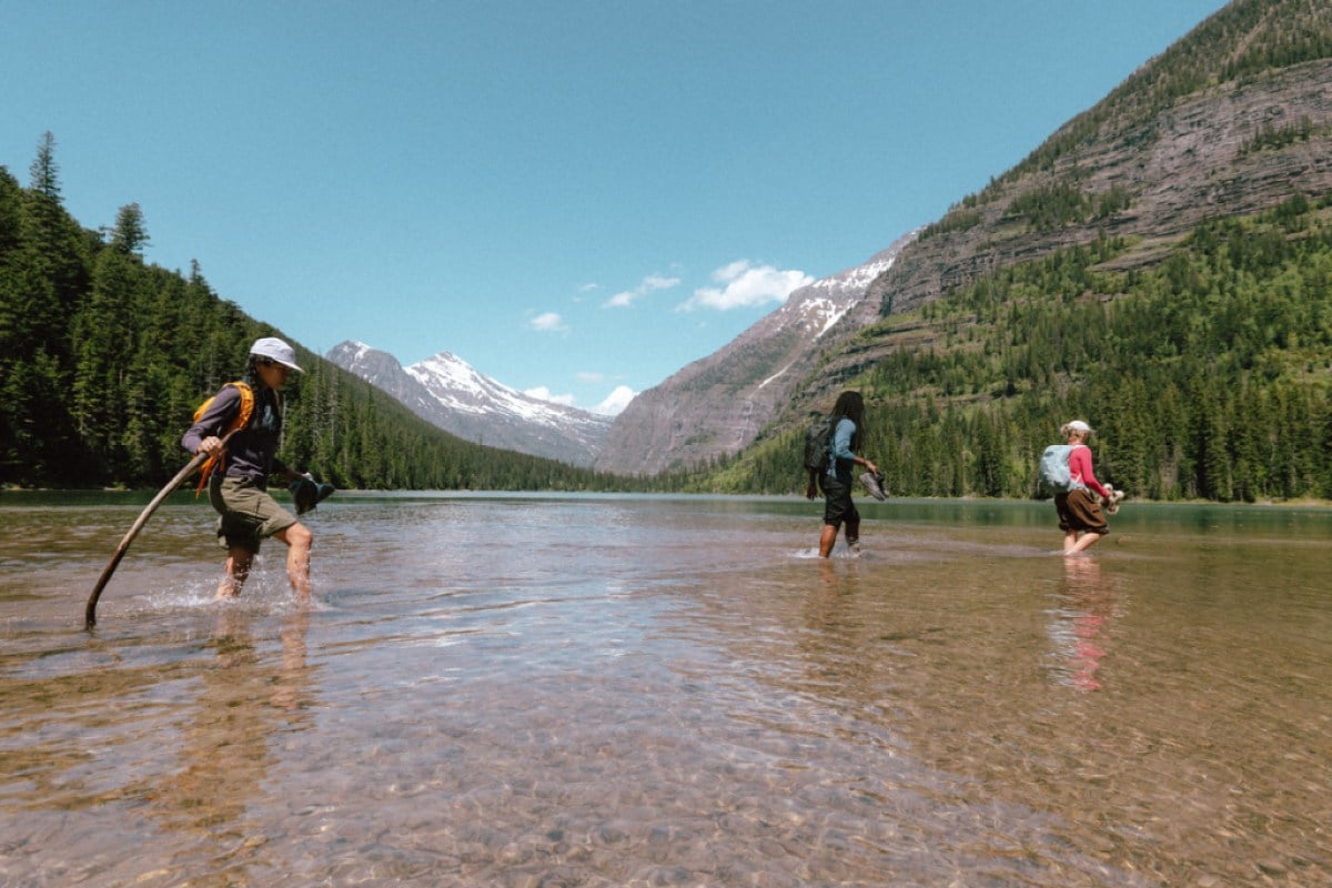 Three people cross a body of water between two peaks.