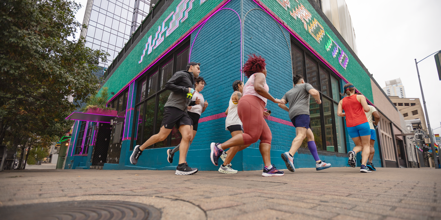 A group of runners wearing different running shorts, tights, tanks and tops in a city setting.