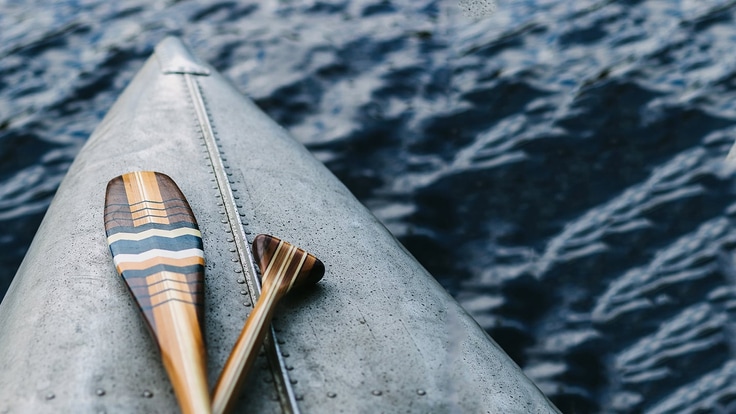 Close up of the front of a canoe with 2 paddles laying on it.