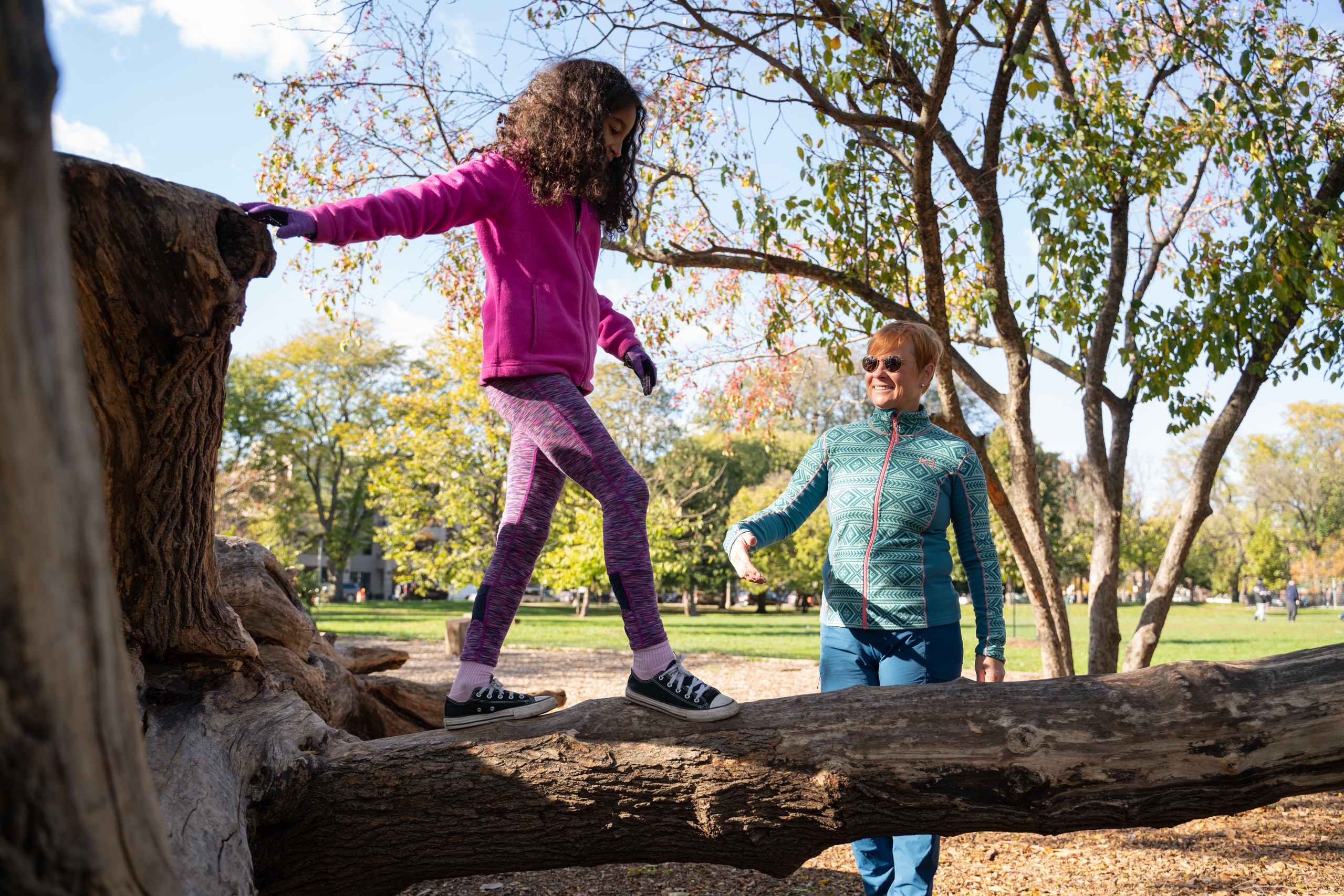 A child walks along the trunk of a downed tree while their parent stands by
